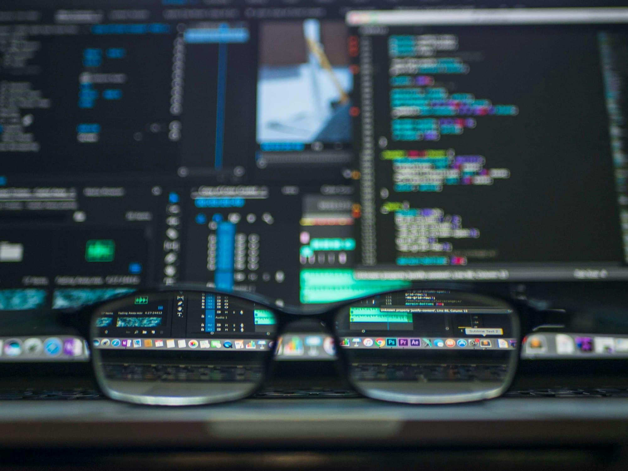 Monitors showing source code behind a pair of glasses